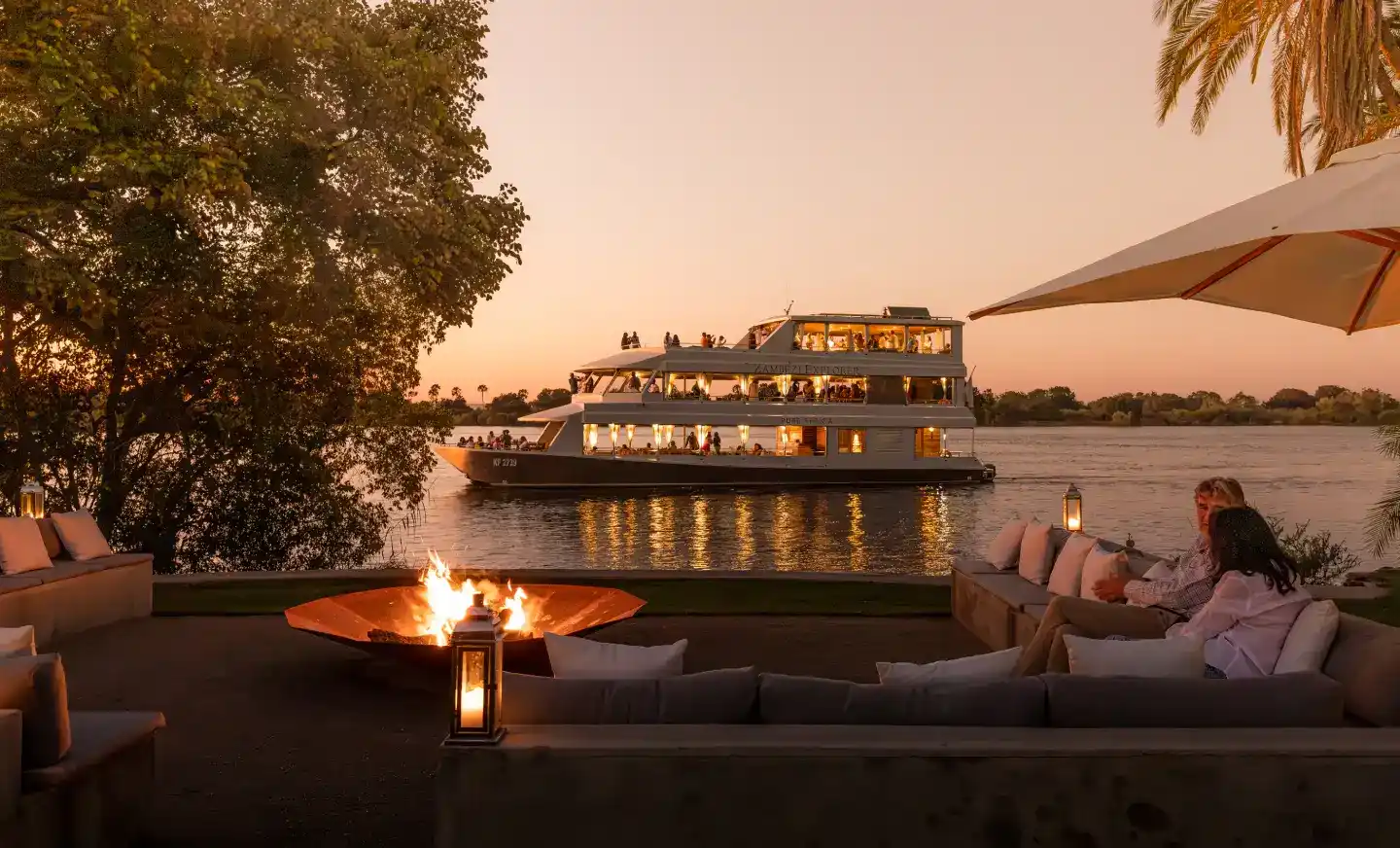 Sunset cruise on the Zambezi River at Victoria Falls, Zimbabwe, with guests watching the sun set while observing hippos, crocodiles, and elephants along the riverbanks